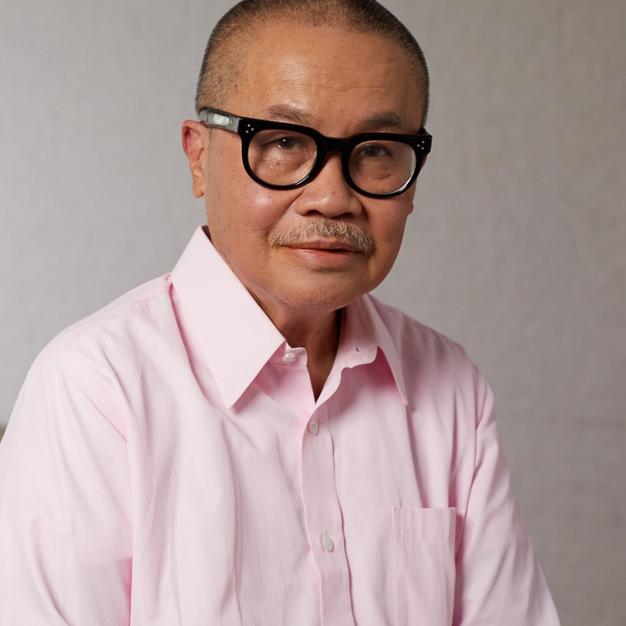 Older man wearing a pink button down and black rimmed glasses smiling for camera.