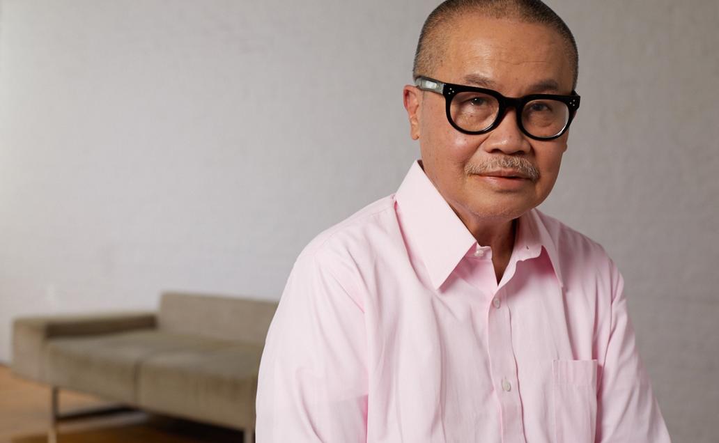 Older man wearing a pink button down and black rimmed glasses smiling for camera.