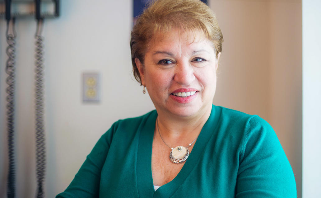 Older women wearing a green sweater smiling for camera in a doctor's office.