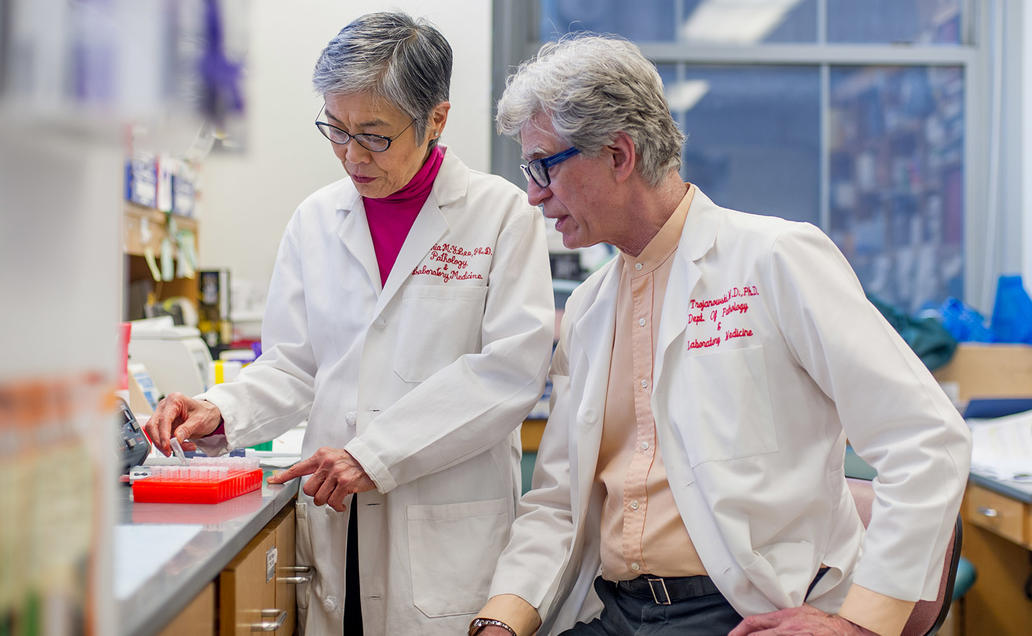 Male and female researcher wearing white lab coats chatting in the lab.