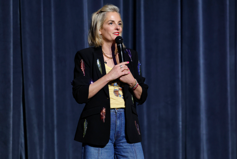 Comedian Maggie Hughes DePalo performing on stage at the 2026 "A Country Thing Happened on the Way to Cure Parkinson's" fundraiser. 