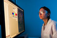 Female researcher in the lab wearing goggles while looking at a scan on the computer screen.