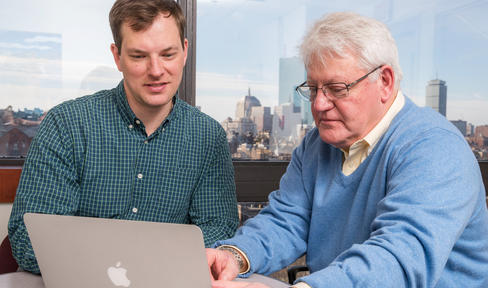 Two people sitting at a table with a laptop.