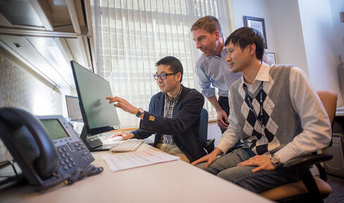 Three men in an office looking at a computer screen.