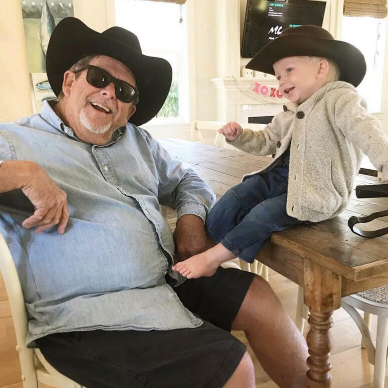 A young boy and his grandfather sit together while wearing matching cowboy hats.