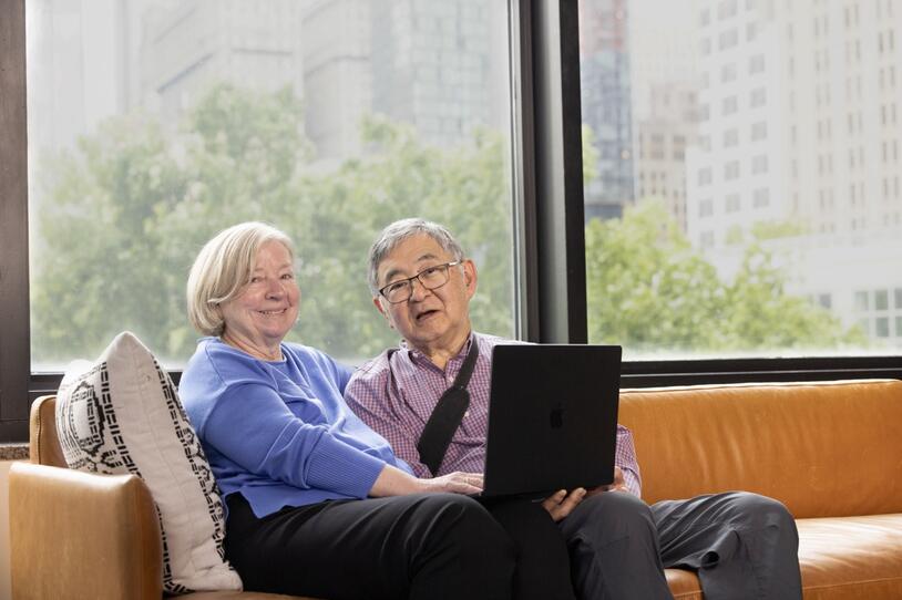 A seated couple smile while sharing a laptop.