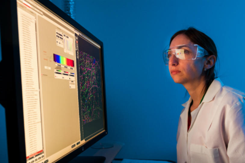 Female researcher in the lab wearing goggles while looking at a scan on the computer screen.