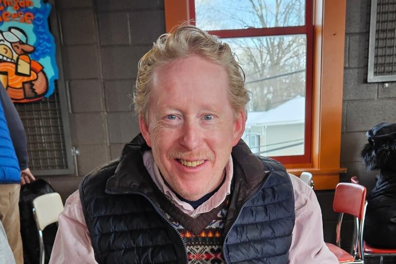 A man smiles indoors at a restaurant.