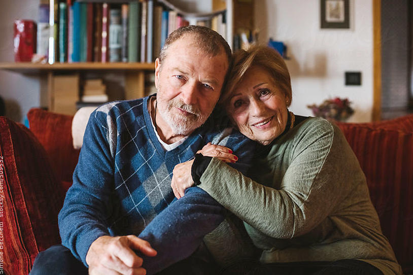 Male and female couple sitting on a couch smiling for the camera.