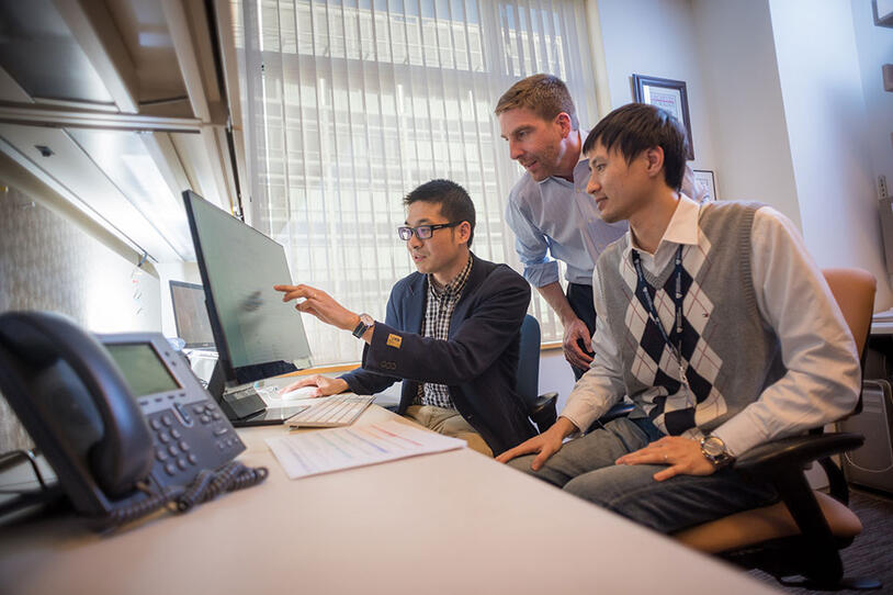 Three men in an office looking at a computer screen.
