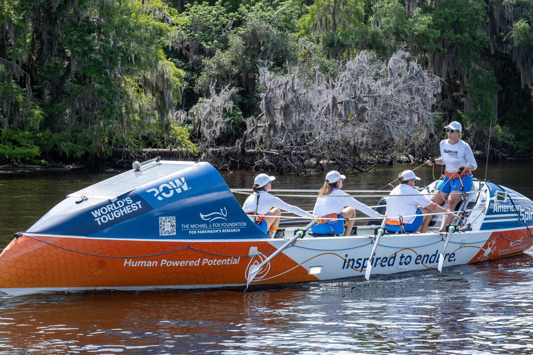 Four members of the Second Wave crew practice rowing the boat on a river.