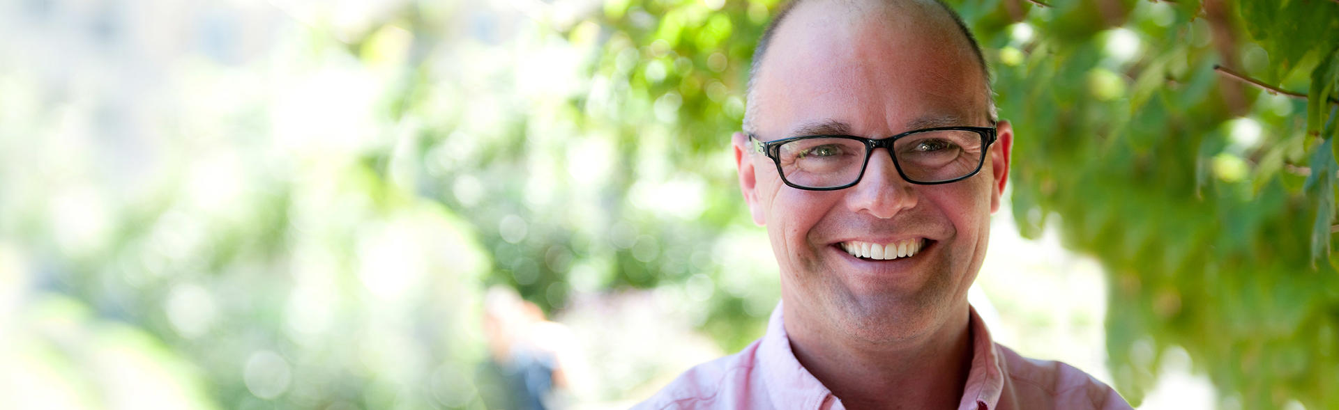 Middle aged white man wearing glasses standing in front of a tree.
