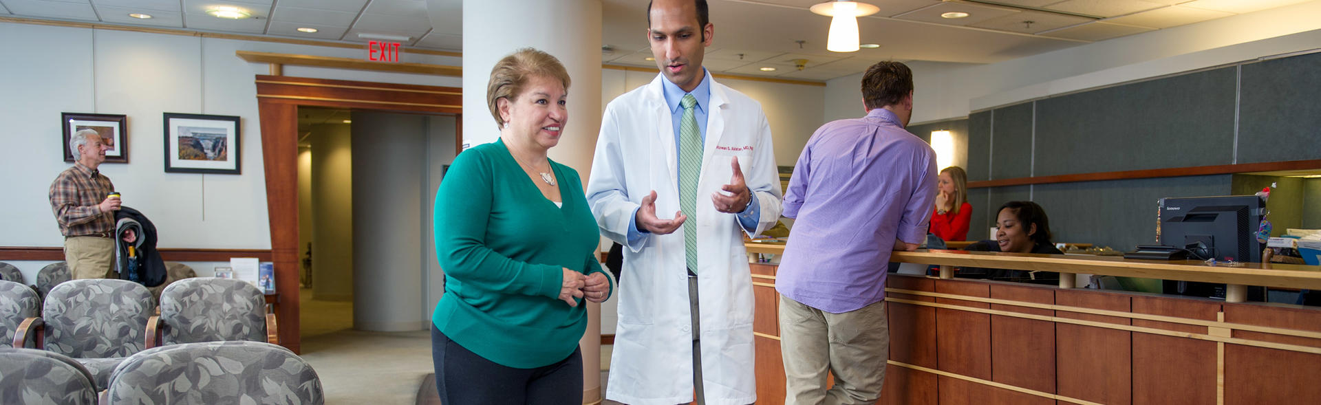 Woman wearing green shirt walking with her male physician through the doctor's office.