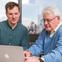 Two people sitting at a table with a laptop.