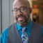 African American male wearing glasses and a blue button down, vest and tie.