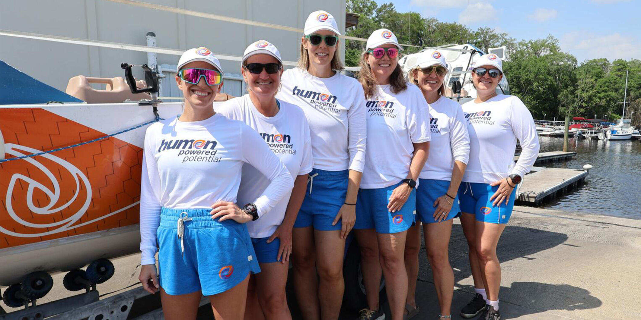 Six members of the all-female rowing crew stand next to their rowboat.
